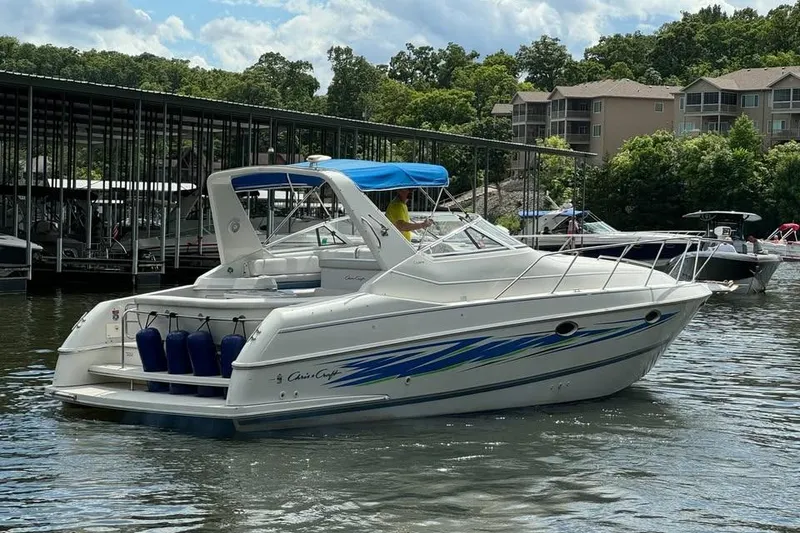 Slide: The Image of 1994 Chris-Craft 322 Crowne boat docked on a sunny day, surrounded by trees and buildings. - 5