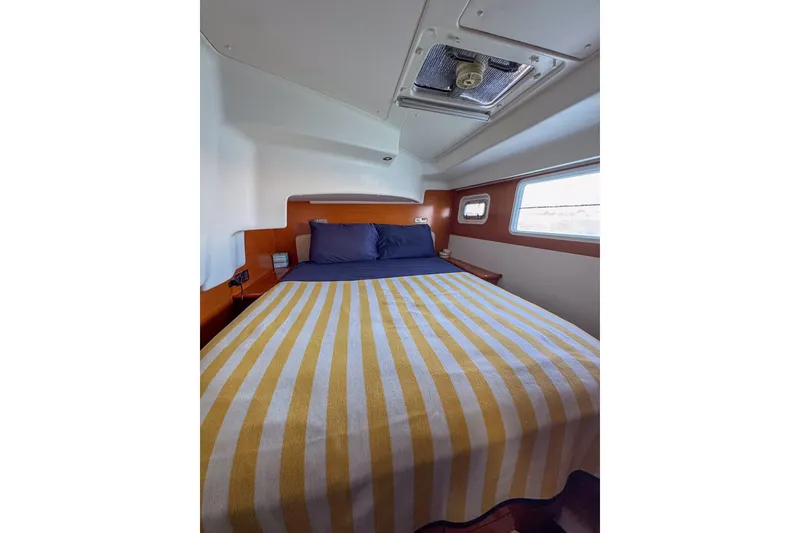 Slide: The Image of Cozy bedroom interior of 2005 Lagoon 440 yacht with striped bedding and porthole window. - 41