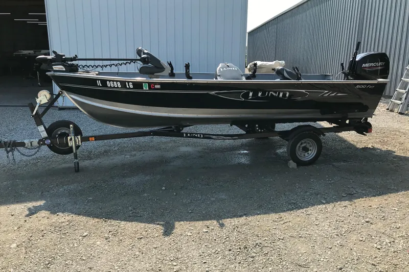 Slide: The Image of 2013 Lund 1600 Fury Tiller boat on trailer, parked outside a metal building. - 3