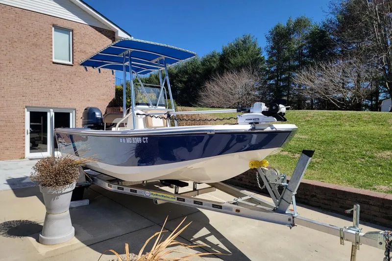 Slide: The Image of 2022 Sundance 20DX boat on trailer, parked beside a brick house under clear blue sky. - 2