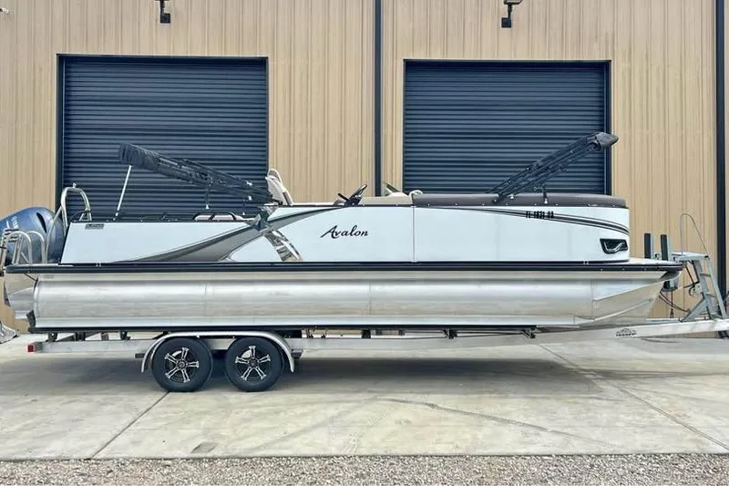 Slide: The Image of 2024 Avalon LSV 2585 pontoon boat on trailer, parked outside a building. - 0