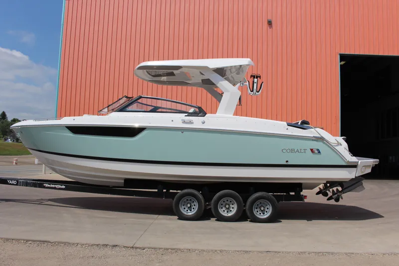 Slide: The Image of 2025 Cobalt R31 Surf boat on trailer, parked near orange building. - 2