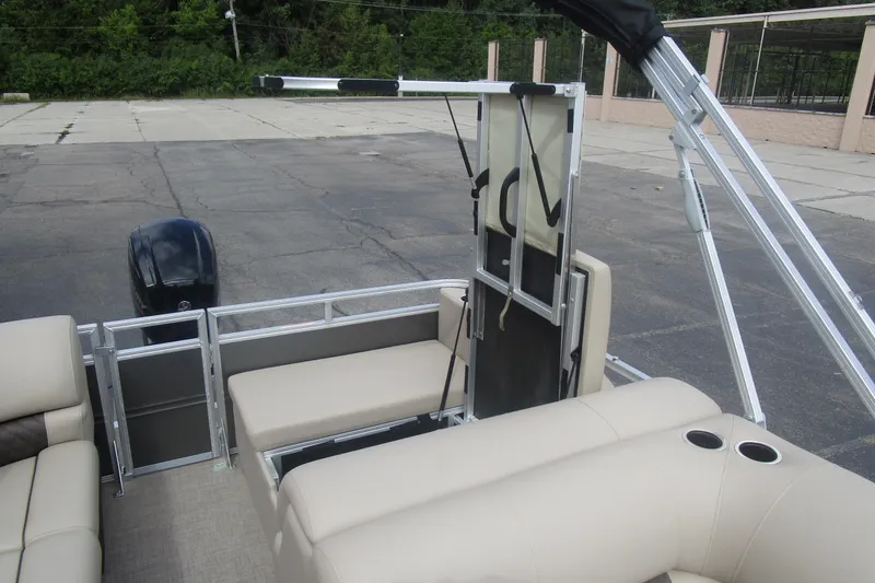 Slide: The Image of 2025 Sun Tracker PB 22 RF pontoon boat interior with seating and motor, parked outdoors. - 13