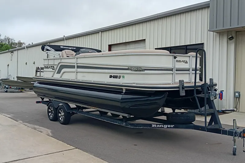Slide: The Image of 2017 Ranger Reata 220C pontoon boat on trailer outside a metal building. - 2