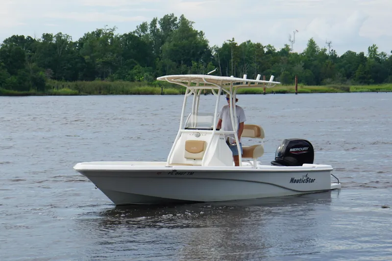 The Image of 2023 NauticStar 215XTS boat on a calm river with lush green background. - 0