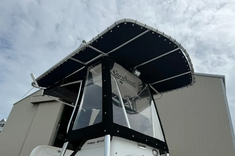 Slide: The Image of 2013 Sea Hunt Triton 210 boat with T-top, docked near a building under cloudy sky. - 5