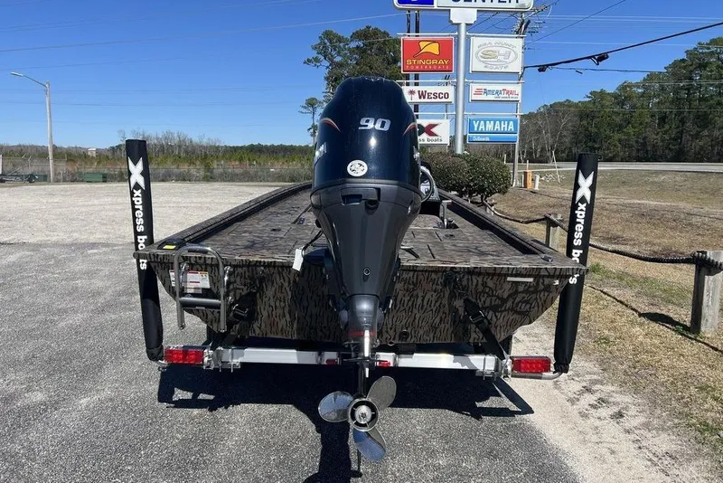 Slide: The Image of 2025 Xpress XP180 boat with 90HP engine, parked outdoors near dealership signs. - 7