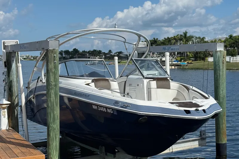 Slide: The Image of 2014 Yamaha Boats 242 Limited S on lift by waterfront, clear sky background. - 2