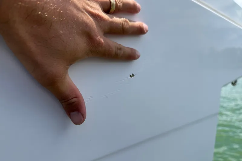 Slide: The Image of Hand inspecting damage on 2023 Axopar 25 Cross Top boat hull. - 12