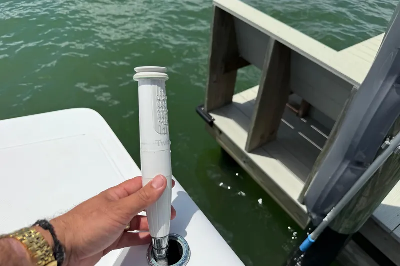 Slide: The Image of Hand holding a white rod on a 2023 Axopar 25 Cross Top boat near a dock. - 27