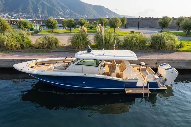 The Image of 2023 Scout 425 LXF boat docked by scenic mountains and lush greenery. - 0