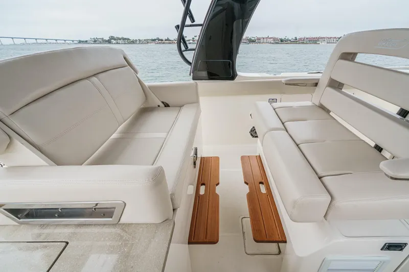 Slide: The Image of 2022 Boston Whaler 350 Realm interior with beige seating and wooden accents, overlooking water. - 56