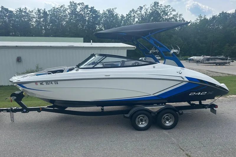 Slide: The Image of 2018 Yamaha 242 X boat on trailer, white and blue design, parked outdoors. - 3