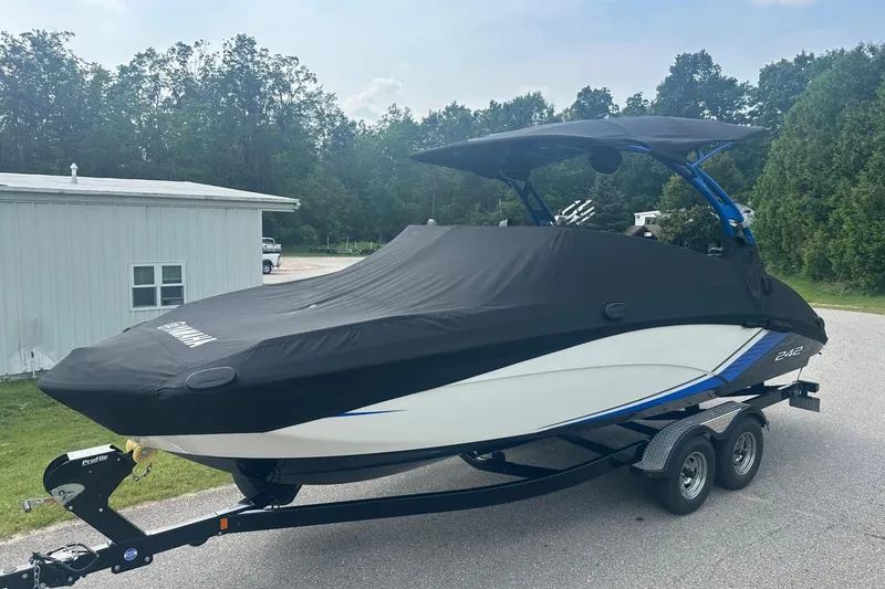 Slide: The Image of 2018 Yamaha 242 X boat covered on trailer, parked outdoors near trees and building. - 30