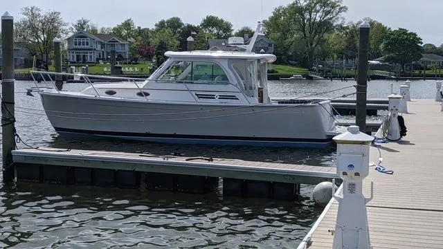 Slide: The Image of 2011 Back Cove 30 boat docked at a marina, surrounded by calm water and greenery. - 0