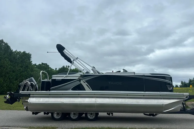 Slide: The Image of 2025 Tahoe 2185 pontoon boat on trailer, parked on roadside under cloudy sky. - 10
