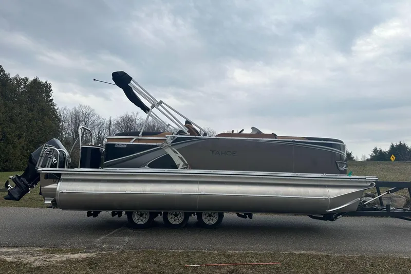 Slide: The Image of 2025 Tahoe 2185 pontoon boat on trailer, parked on roadside under cloudy sky. - 7