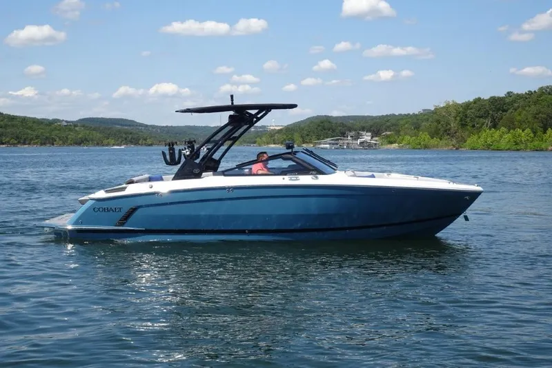Slide: The Image of 2026 Cobalt R8 Surf boat on a scenic lake with blue skies and lush greenery. - 2