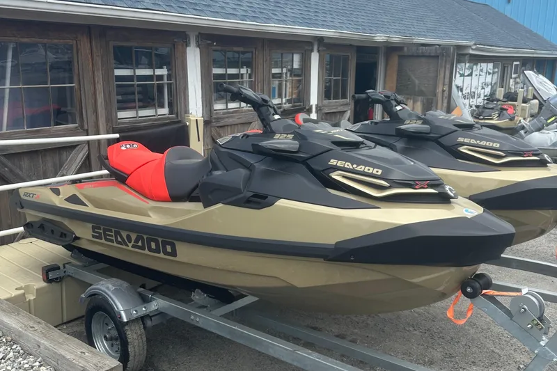 Slide: The Image of 2025 Sea-Doo RXT-X 325 jet ski on trailer, parked outside wooden building. - 4