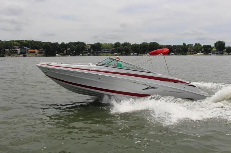 The Image of 2022 Crownline 240 SS speedboat cruising on a lake with red accents and canopy. - 1
