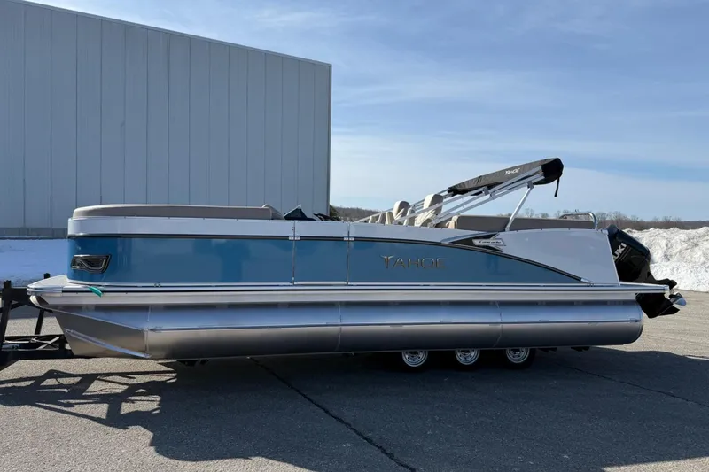 Slide: The Image of 2025 Tahoe 2385 pontoon boat with blue and silver design, parked outdoors. - 1