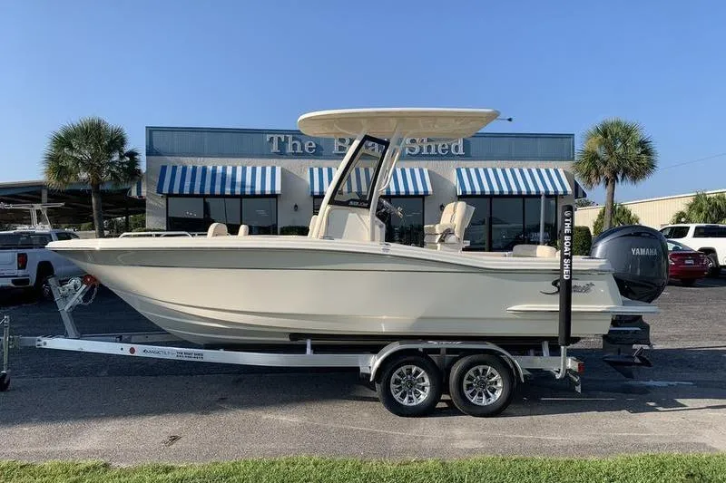 The Image of 2026 Scout 215 XSF boat on trailer, parked outside a building with striped awnings. - 1