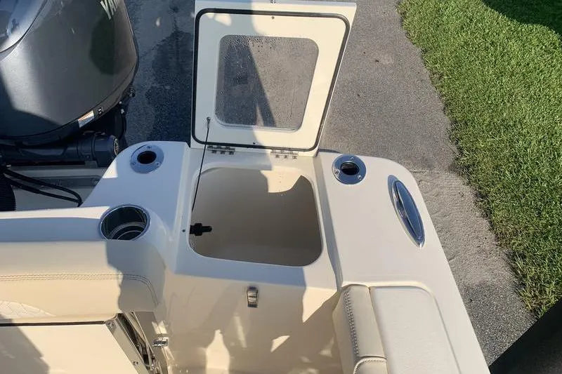 Slide: The Image of 2026 Scout 215 XSF boat with open storage compartment and motor, parked on pavement. - 14