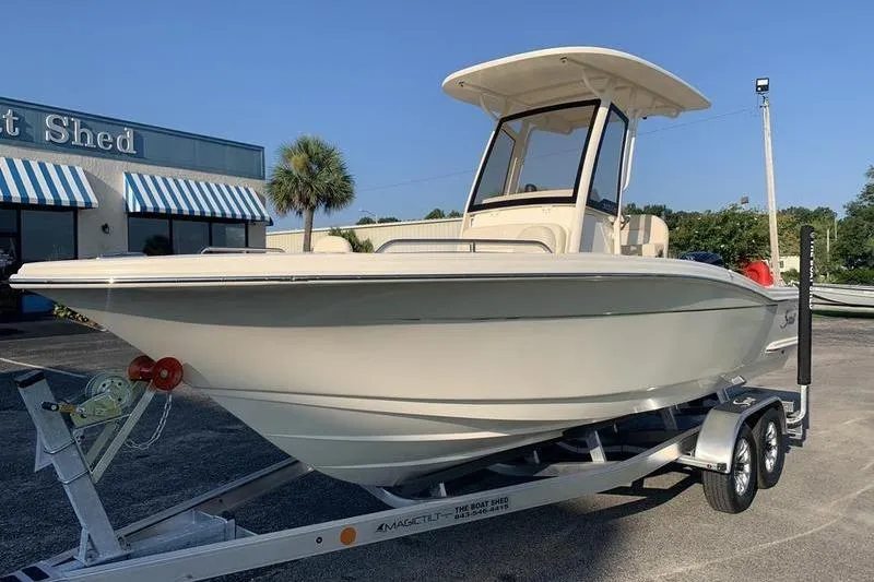 Slide: The Image of 2026 Scout 215 XSF boat on trailer, parked outside a building with striped awnings. - 8