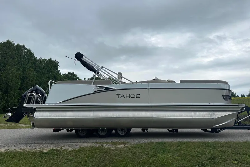 Slide: The Image of 2025 Tahoe 2385 pontoon boat on trailer, parked on roadside with cloudy sky backdrop. - 10