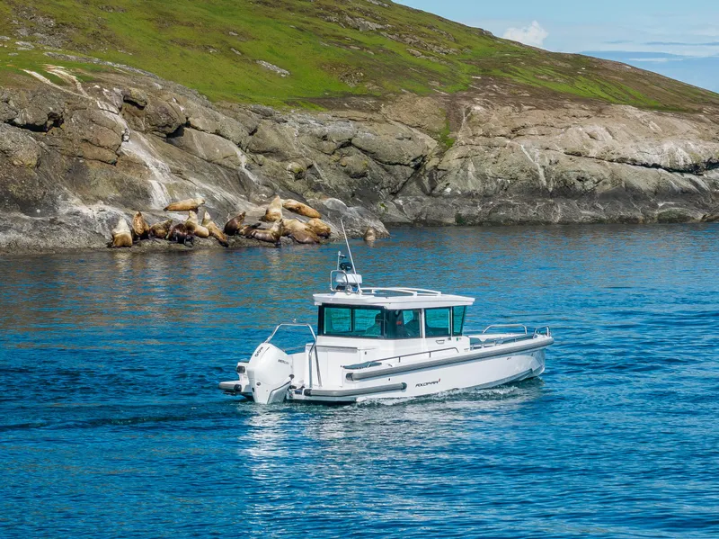 Slide: The Image of 2022 Axopar 28 boat cruising near rocky shoreline in clear blue water. - 26