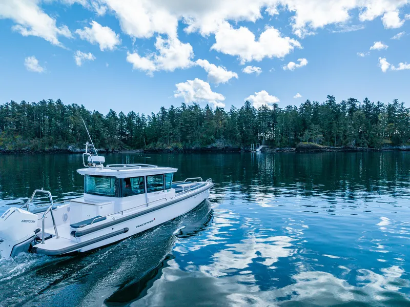Slide: The Image of 2022 Axopar 28 boat cruising on a serene lake with forested shoreline. - 6