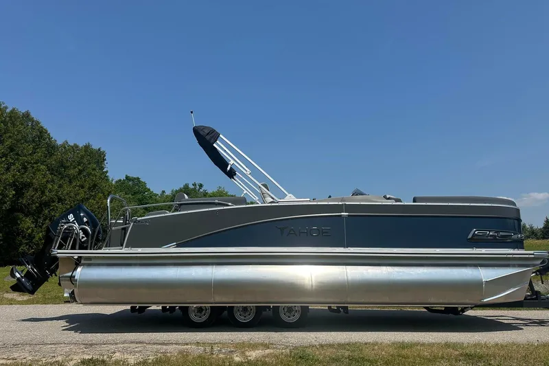 Slide: The Image of 2025 Tahoe 2385 pontoon boat on trailer, parked outdoors under clear blue sky. - 3