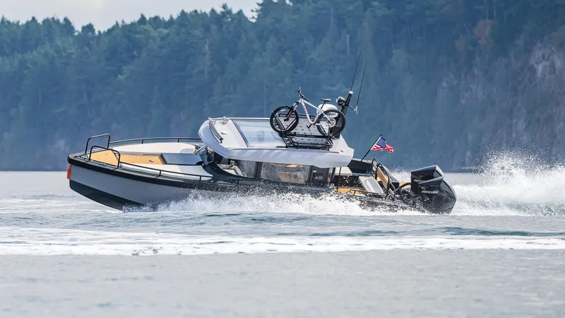Slide: The Image of 2023 Arksen 30 boat cruising with a motorcycle on deck, set against a forested shoreline. - 1