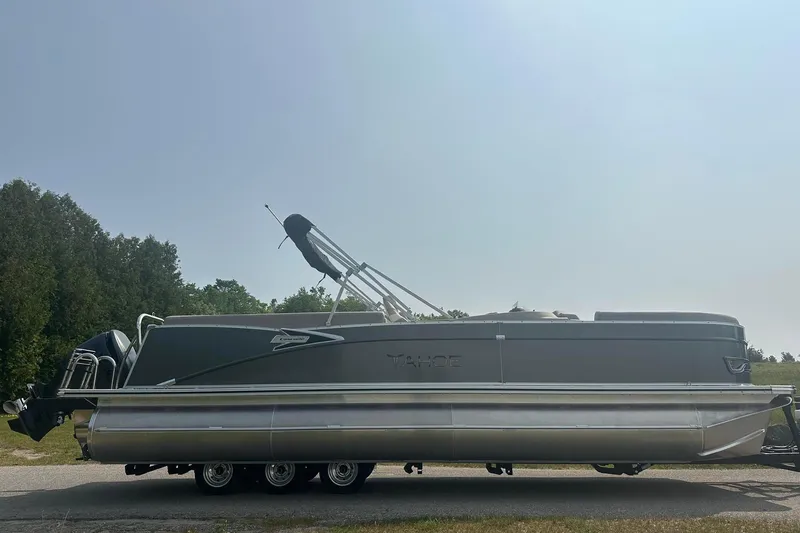 Slide: The Image of 2025 Tahoe 2585 pontoon boat on trailer, parked outdoors under clear sky. - 6