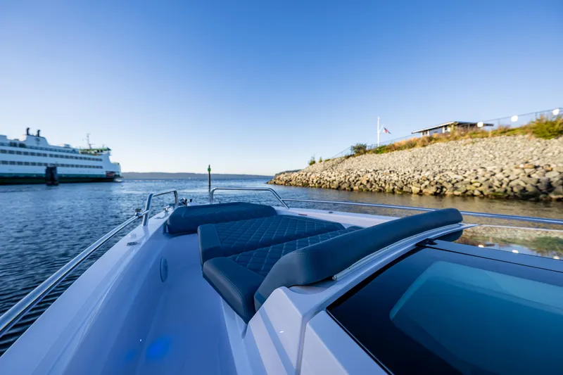 Slide: The Image of Axopar 37 XC 2022 boat with blue seating, near a ferry and rocky shoreline. - 12