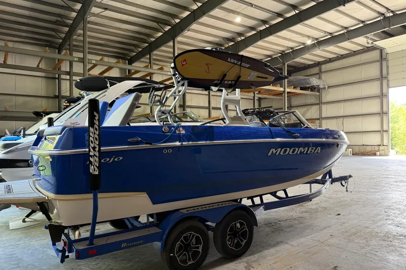 Slide: The Image of 2023 Moomba Mojo boat in a warehouse, blue exterior, on a trailer. - 2
