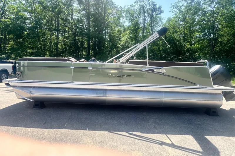 Slide: The Image of 2025 Tahoe 2585 pontoon boat parked on pavement with forest background. - 1