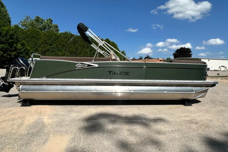 Slide: The Image of 2025 Tahoe 2585 pontoon boat with green exterior, parked outdoors under a blue sky. - 6
