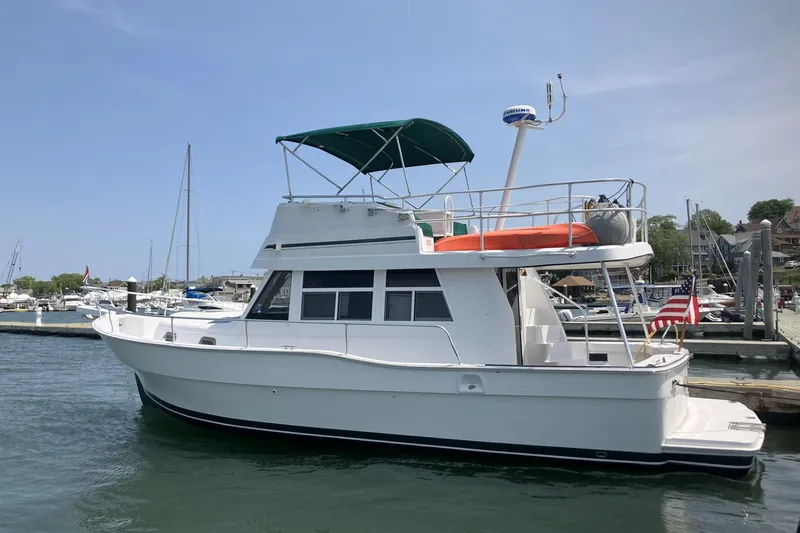 The Image of 1999 Mainship 350 Trawler docked at marina, featuring green canopy and American flag. - 0