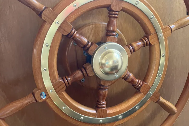 Slide: The Image of Wooden ship wheel of a 1999 Mainship 350 Trawler, featuring brass accents. - 14