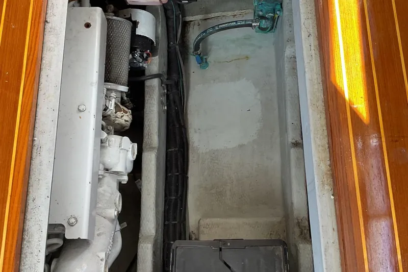 Slide: The Image of Engine compartment of a 1999 Mainship 350 Trawler, showcasing mechanical components and wooden flooring. - 23