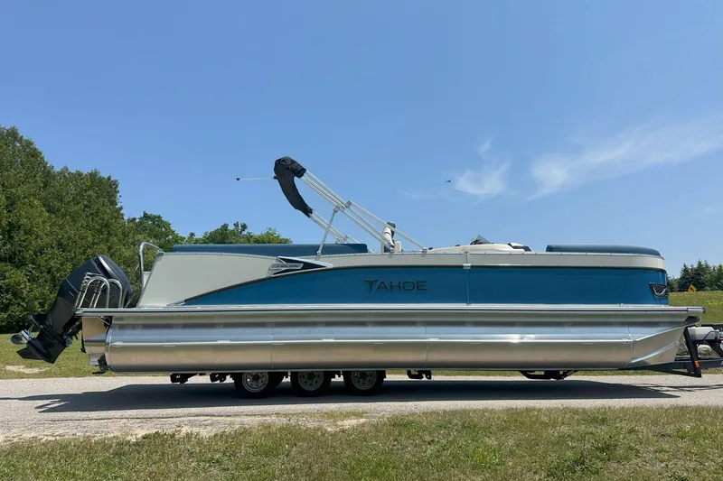 Slide: The Image of 2025 Tahoe 2585 pontoon boat on trailer, parked outdoors under clear blue sky. - 10