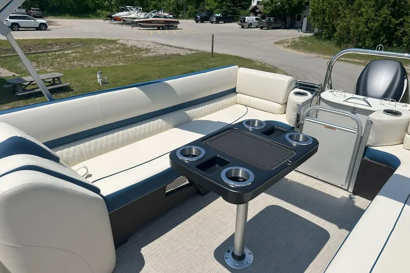 Slide: The Image of 2025 Tahoe 2585 pontoon boat interior with seating and table, parked near a marina. - 22