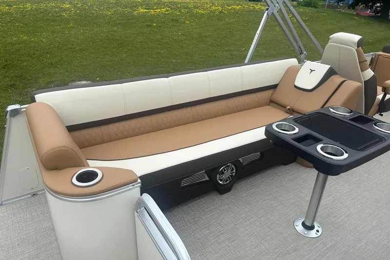 Slide: The Image of Luxurious seating on 2025 Tahoe 2585 boat with cup holders and table, set against grassy backdrop. - 14