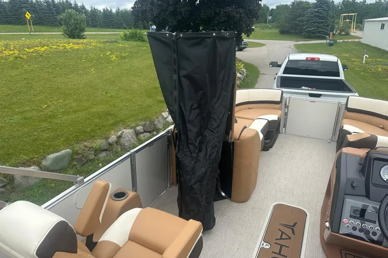 Slide: The Image of 2025 Tahoe 2585 pontoon boat interior with seating and steering console, parked near a grassy area. - 33