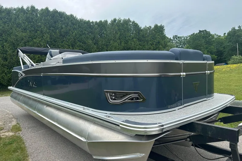 Slide: The Image of 2025 Tahoe 2585 pontoon boat on trailer, parked outdoors with lush greenery. - 10