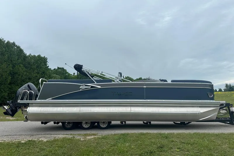 Slide: The Image of 2025 Tahoe 2585 pontoon boat on trailer, parked on roadside with trees in background. - 9