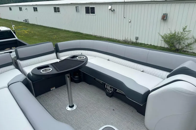 Slide: The Image of 2025 Tahoe 2585 boat interior with gray seating and table, parked near a building. - 14