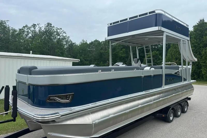 Slide: The Image of 2025 Tahoe 2585 pontoon boat with sleek design on a trailer, surrounded by greenery. - 3