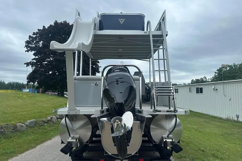 Slide: The Image of 2025 Tahoe 2585 pontoon boat with slide and ladder, parked on grass under cloudy sky. - 5